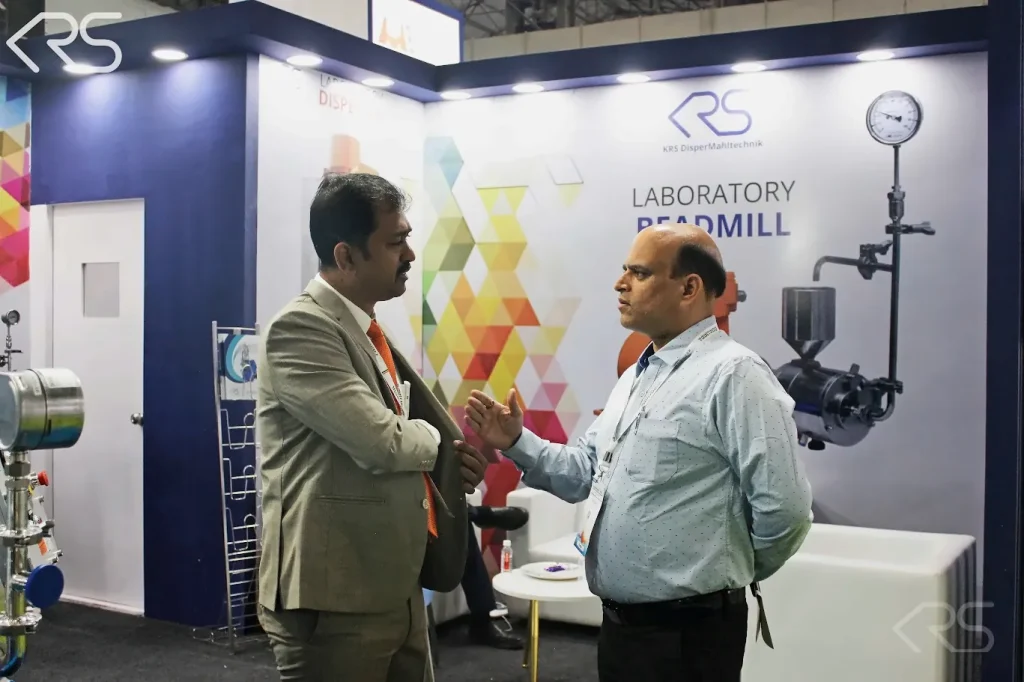 Discussion at the KRS stand at Paint India 2026 beside laboratory bead mill display